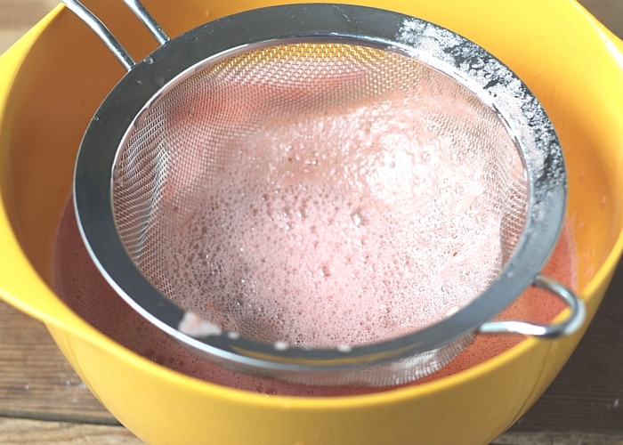 a strainer in a yellow bowl after Watermelon punch has been poured through the strainer