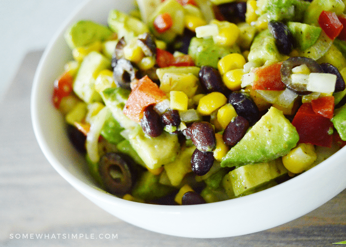 a close up of a bowl filled with this texas caviar recipe. The ingrdients you can see in the bowl are corn, avocado, tomatoes, red bell pepper and olives.