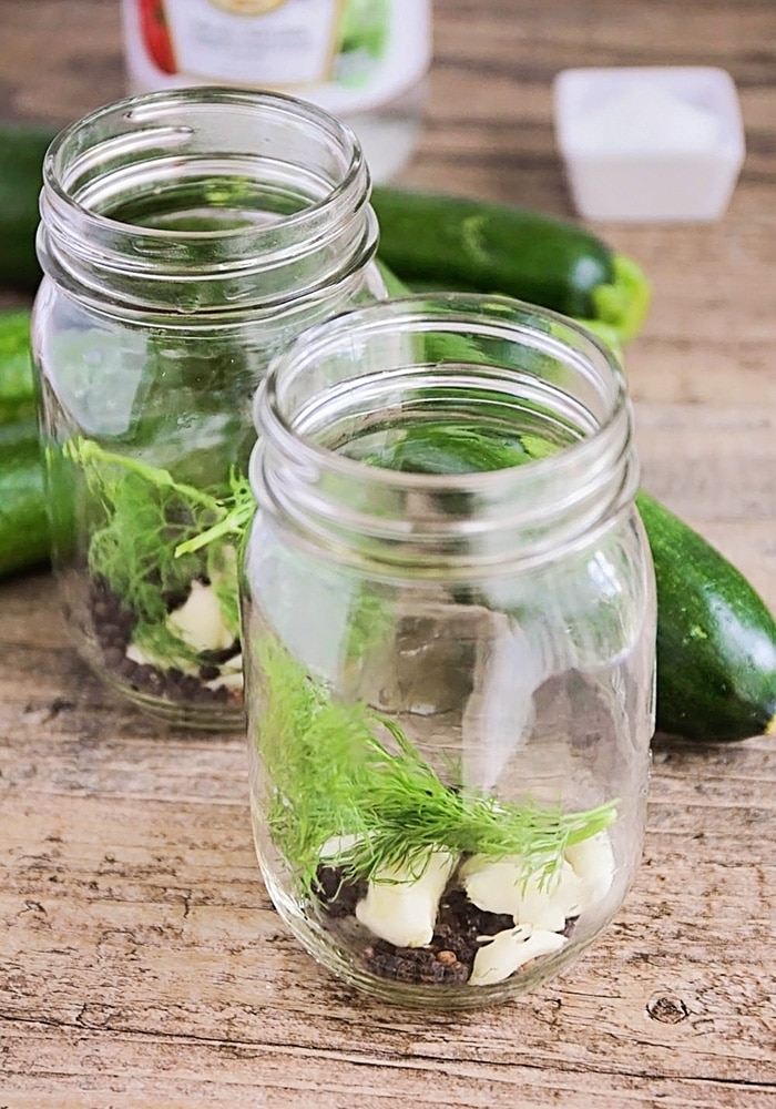 mason jars with garlic dill and peppercorns at the bottom