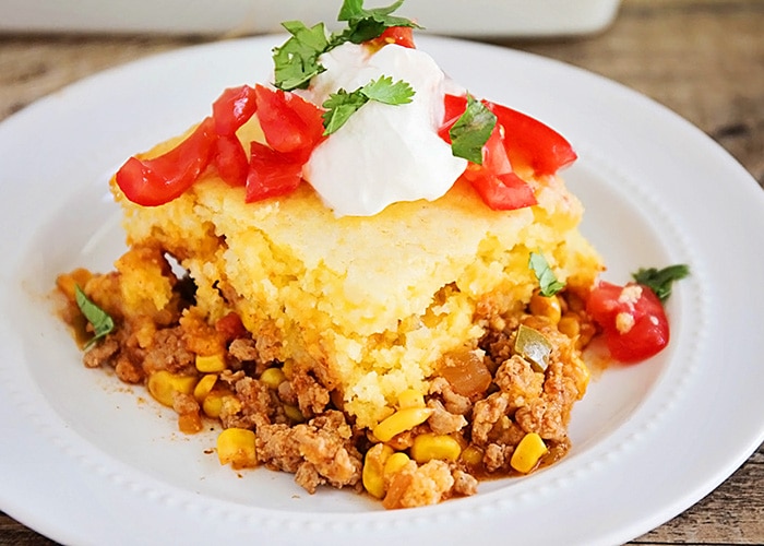 a serving of this easy tamale pie recipe with cornbread and cheese and topped with tomatoes and sour cream on a white plate