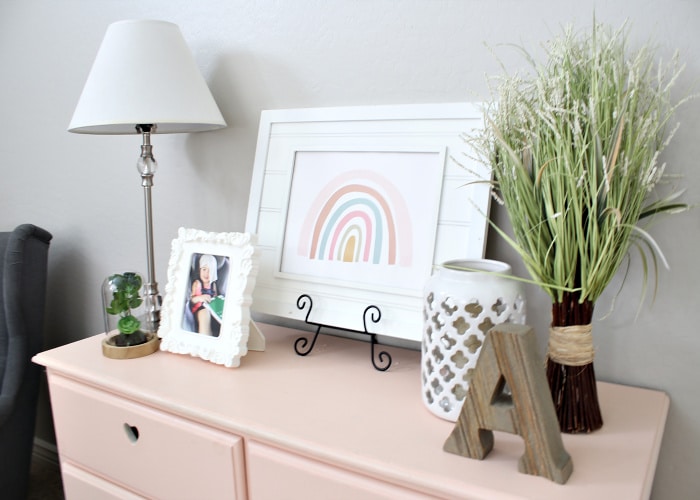 a pink dresser with pictures, a lamp, a plant and a wooden letter A on top