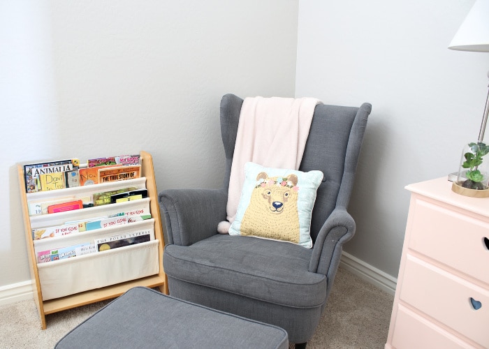 a gray chair with a matching ottoman in the corner of a room next to a small book shelf and a pink dresser