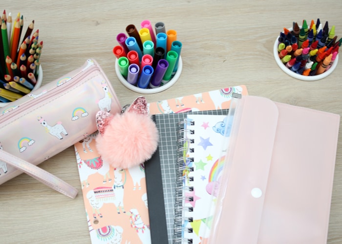 looking down on a desk with colored pencils, markers, crayons and notebooks on top