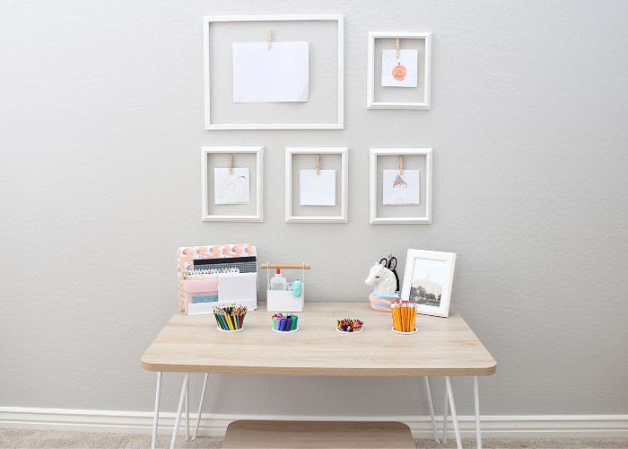 a wooden art table against a wall with picture frames hanging in front of it on the wall