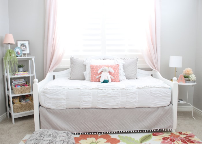 a little girl's bed with several pillows and a stuffed bunny on the bed