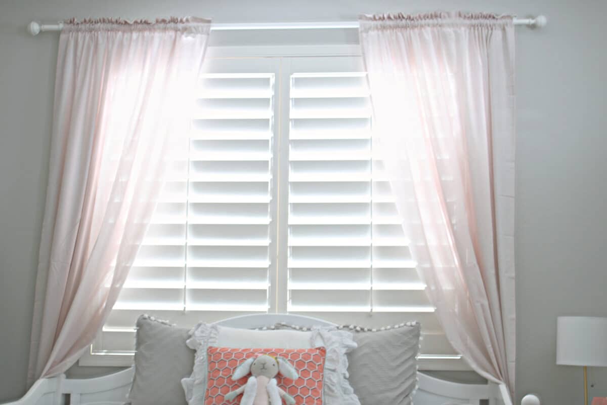 pink curtains hanging in front of a window covered by white shutters