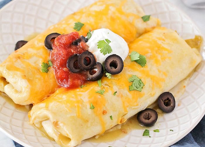 a plate with two Green Chili Chicken Enchiladas topped with cheese, salsa, olives and sour cream