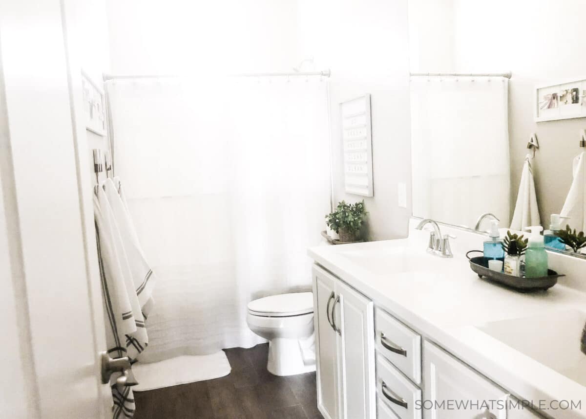 a bathroom with white cabinets and a white counter top, that has towels hanging from a rack and a white ruffled shower curtain