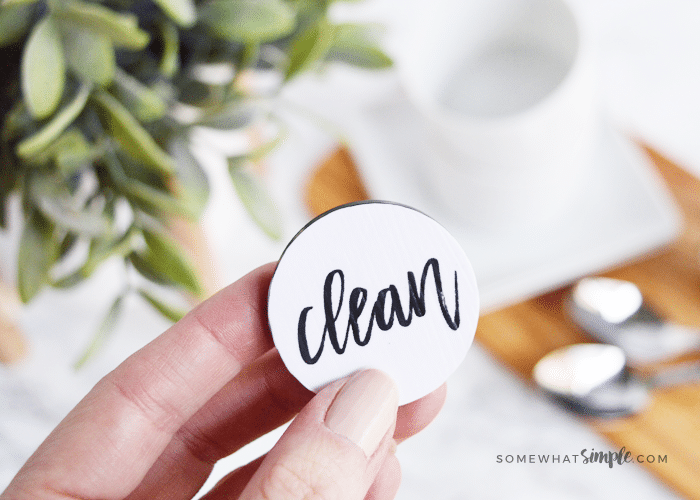 a hand holding up a dishwasher magnet with the white side that says clean on it facing the camera