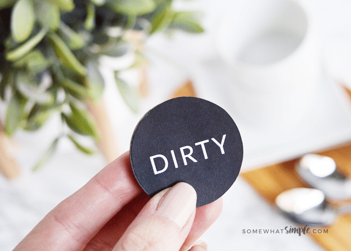 a hand holding up a dishwasher magnet with the black side that says dirty on it facing the camera
