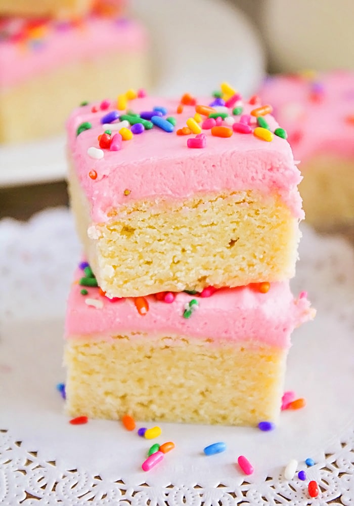 Stack of sugar cookies cut into squares with hot pick frosting and rainbow sprinkles