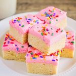 a plate of old fashioned sugar cookies topped with pink frosting and colorful sprinkles