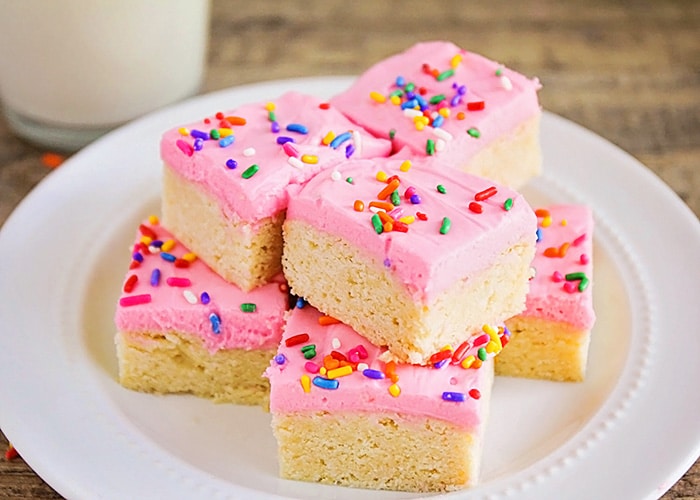 a plate of old fashioned sugar cookies topped with pink frosting and colorful sprinkles