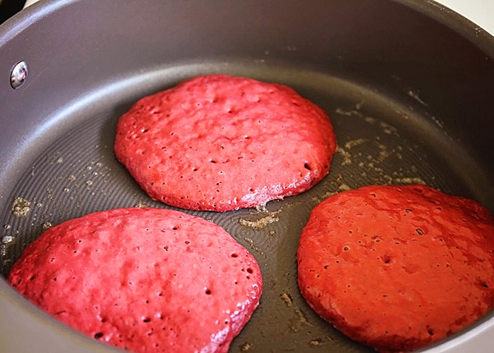 a frying pan with three Red Velvet Pancakes cooking in it