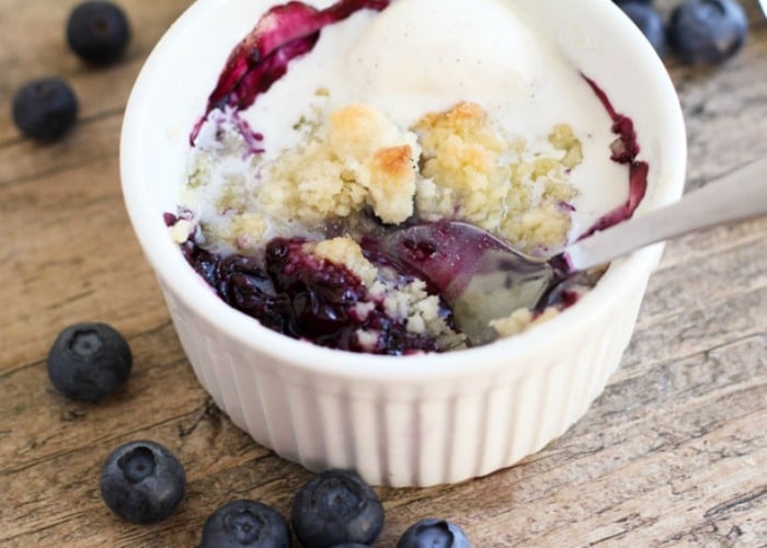 a ramekin filled with this blueberry crumble recipe topped with a scoop of vanilla ice cream