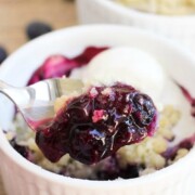 a spoon scooping out a bite of blueberry crumble out of an individual serving in a white ramekin