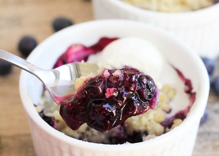 a spoon scooping out a bite of blueberry crumble out of an individual serving in a white ramekin