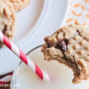 a peanut butter cookie with chocolate chip with a bite taken out of it sitting on the rim of a glass of milk