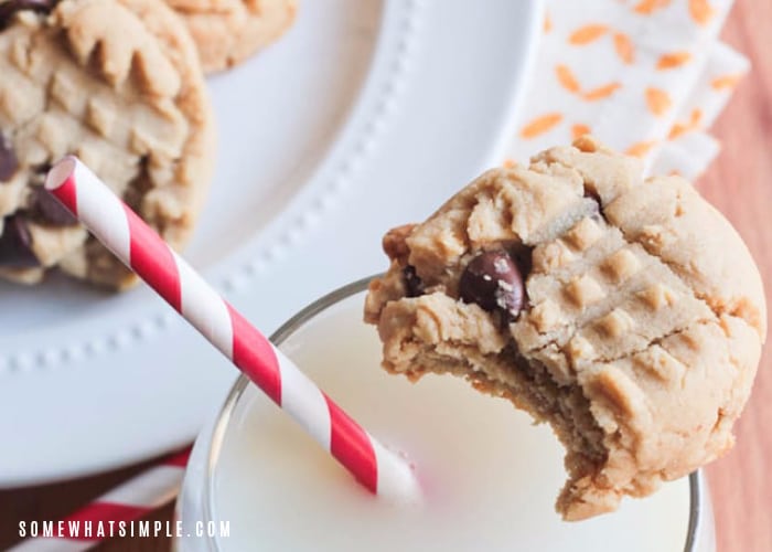 a peanut butter cookie with chocolate chip with a bite taken out of it sitting on the rim of a glass of milk