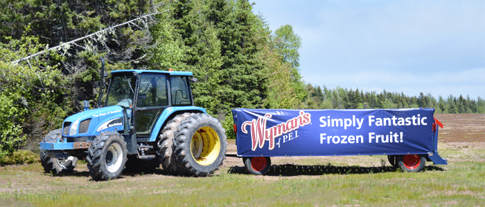 a tractor pulling a trailer with a Wyman's of Maine sign
