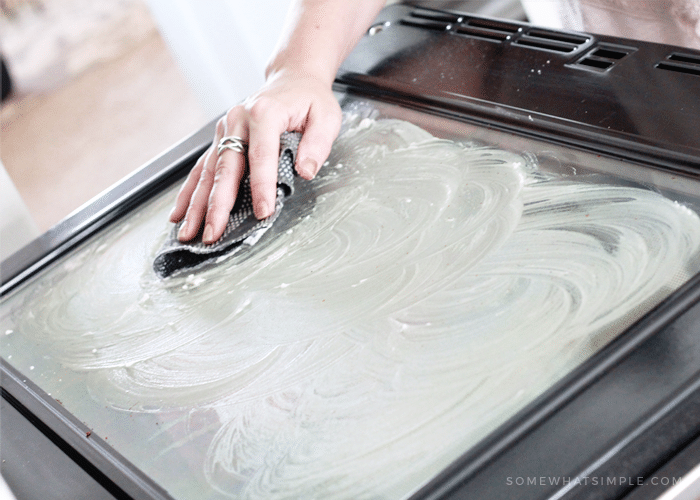 scrubbing the baking soda mixture on an oven glass door is how to clean your oven