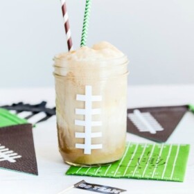 a mason jar painted to look like a football with a foaming drink inside