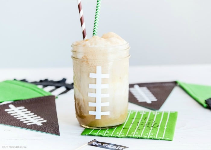 a mason jar painted to look like a football with a foaming drink inside