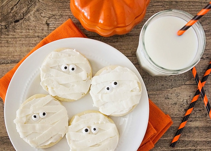 Halloween Mummy sugar Cookies on a plate next to a glass of milk