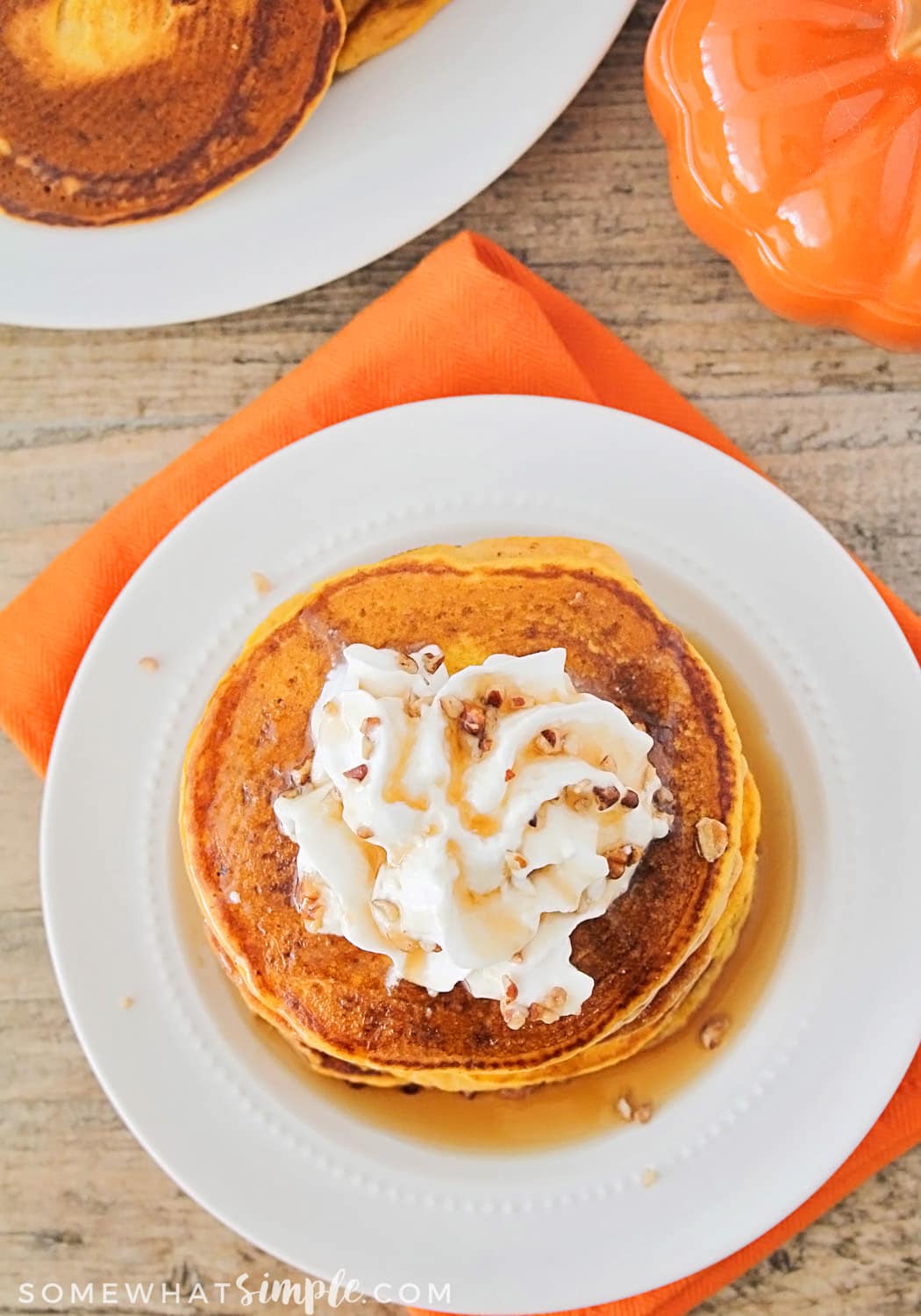 easy fluffy Pumpkin Pancakes Recipe on a white plate topped with whipped cream on a white plate sitting on top of an orange napkin