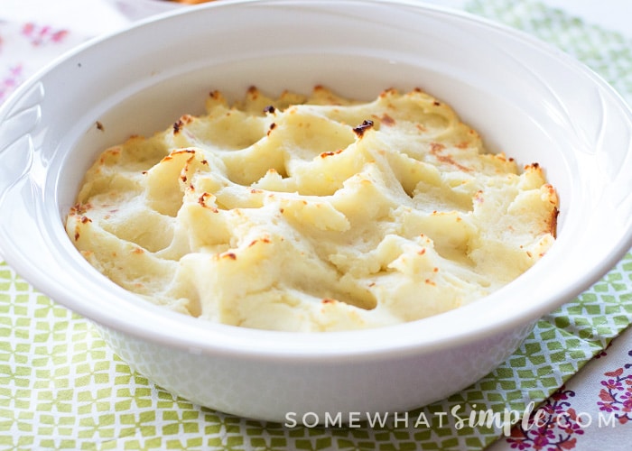 a white bowl filled with garlic parmesan mashed potatoes. The potatoes have just come from the oven so the top of the potatoes are a golden brown color.