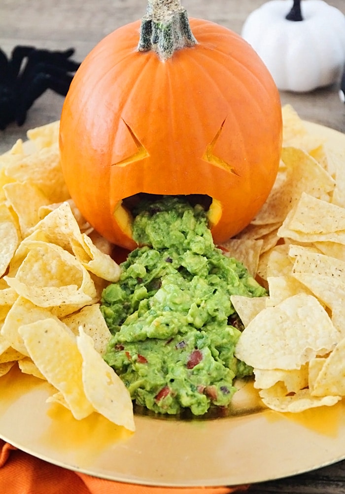 a pumpkin puking out guacamole on a serving platter with chips