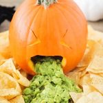 a barfing pumpkin with guacamole coming out of it's mouth with tortilla chips spread all around