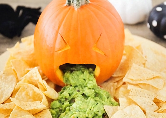 a barfing pumpkin with guacamole coming out of it's mouth with tortilla chips spread all around