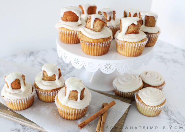 a dozen cinnamon rolls on the counter and on a cake stand