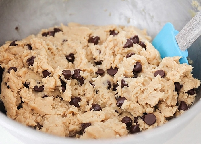 dough for the chocolate chip cookie base being stirred in a metal bowl with a blue spatula