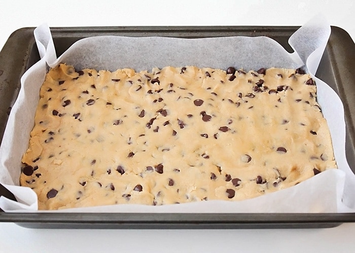 the cookie bar dough base spread out in a parchment paper lined baking pan