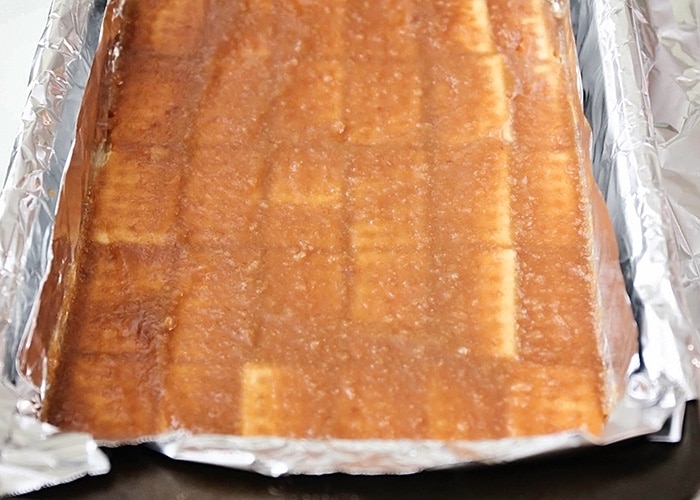 a baking sheet with club crackers topped with a butter mixture