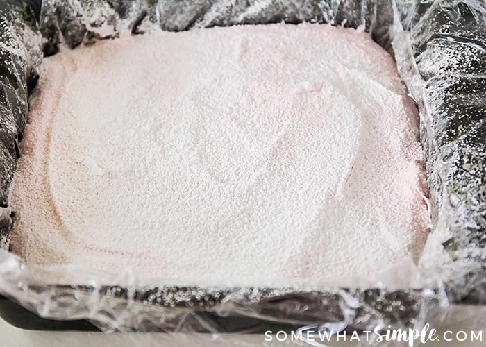 a pan filled with the pink mixture for homemade marshmallows covered in powdered sugar
