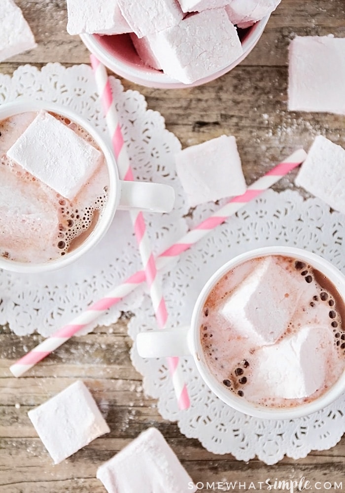 looking down on two mugs of hot chocolate and a pink bowl with Homemade Strawberry Marshmallows inside