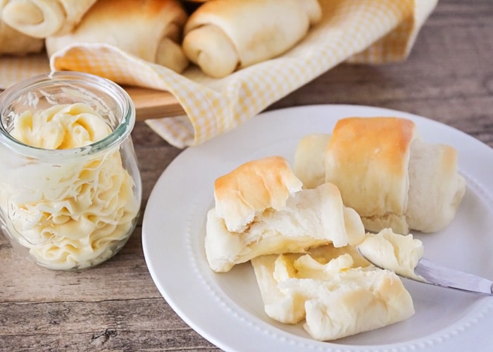 two lion house rolls on a white plate with a knife that has butter on it laying on the plate. 