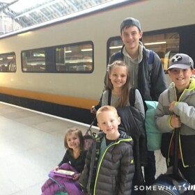 five children standing on the Eurostar train platform in London. Behind them is a high speed train that is headed to Paris.