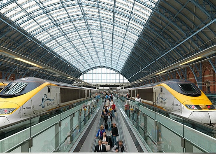 Inside St. Pancras station in London with a Eurostar bullet train on each side of the platform with a trail of people riding the moving walkway in between the trains. These trains are the best way to travel throughout Europe.