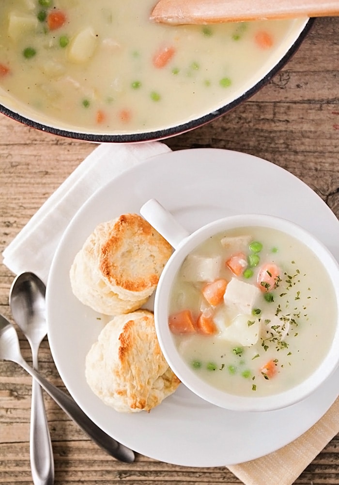 a pot and a cup filled with soup made with chicken and vegetables