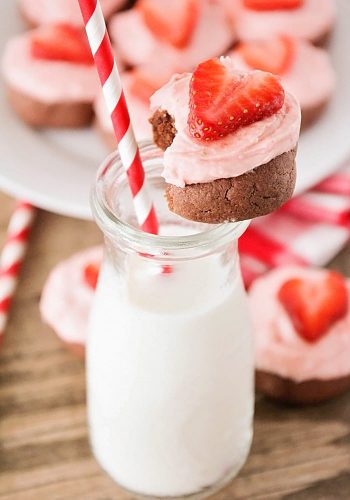 chocolate sugar cookie sitting on top of a tall glass of milk with a red straw