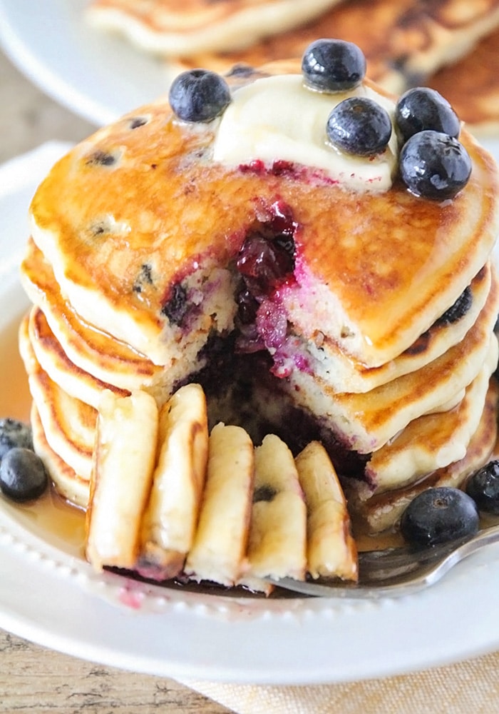 a stack of blueberry pancakes with a wedge cut out of the side of the stack