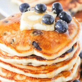 a stack of lemon blueberry pancakes topped with a pad of butter, syrup and fresh blueberries