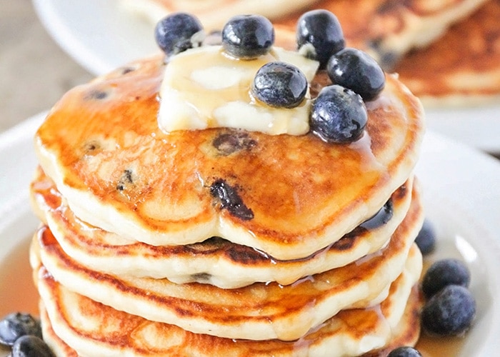 a stack of lemon blueberry pancakes topped with a pad of butter, syrup and fresh blueberries