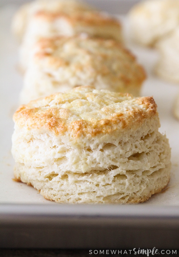 a close up of a homemade golden brown biscuit on a baking sheet. More biscuits are in the background.