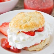 a piece of strawberry shortcake made with a biscuit and filled with sliced strawberries and whipped cream on a white plate. Additional strawberry slices are on the plate.
