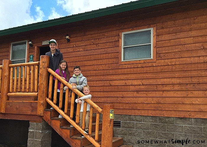 4 cute children next to a mountain cabin